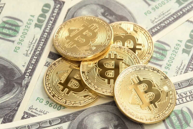 pile of bitcoins on one hundred dollar banknotes